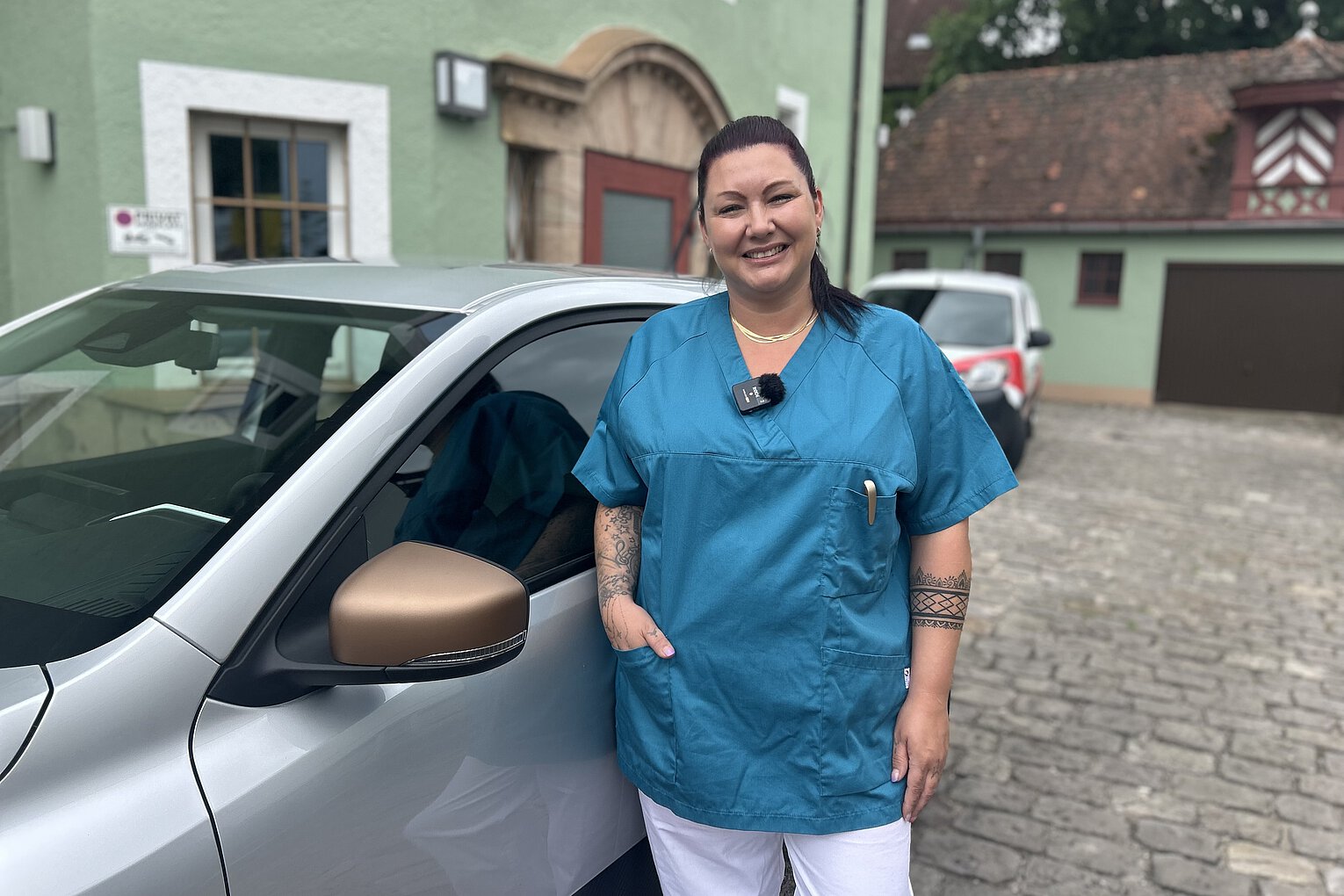 Frau in blauem Pflege-Kasack vor einem Auto